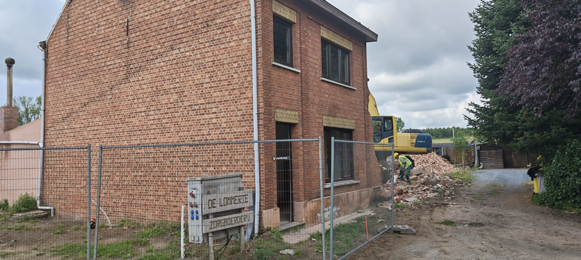 Bakstenen woning klaar voor afbraak met werfhek en graafmachine