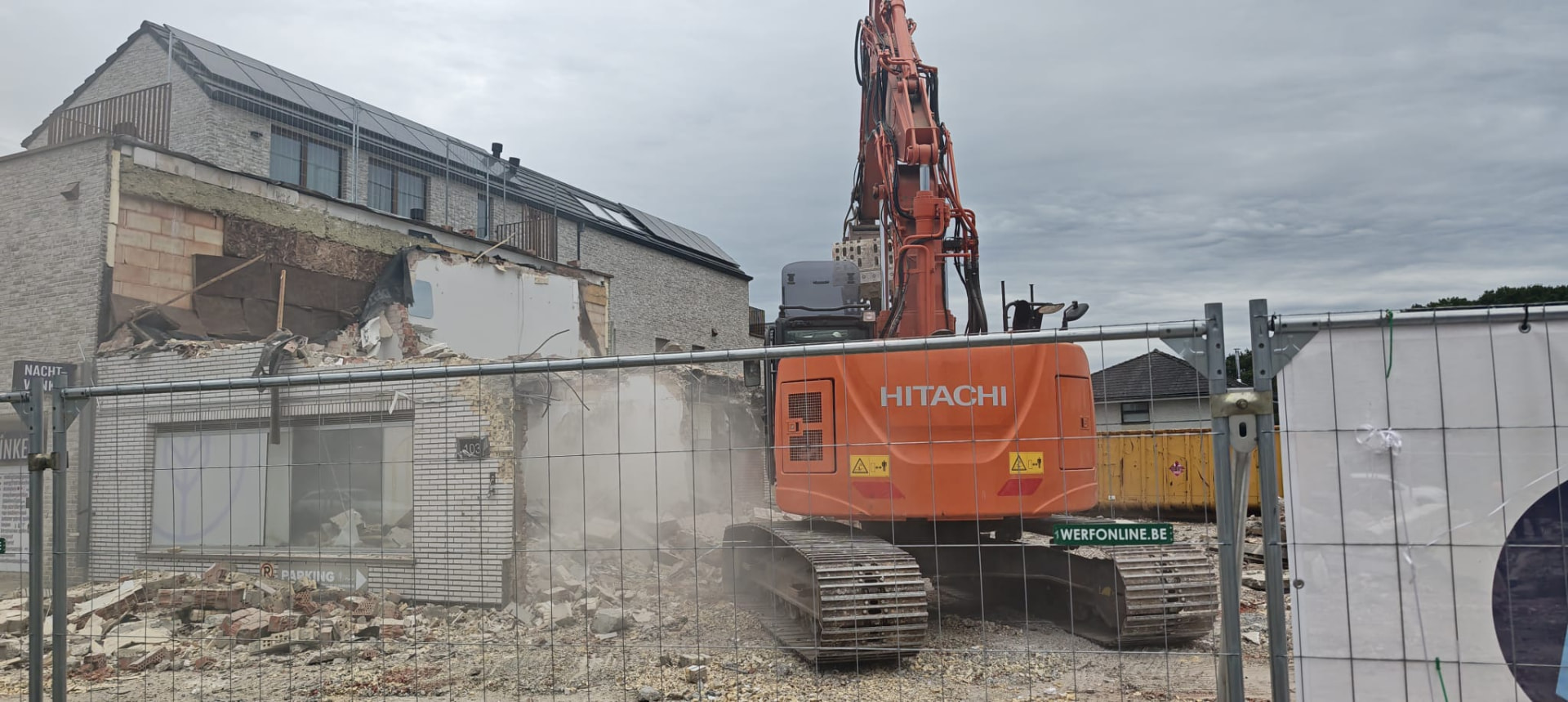Hitachi-graafmachine op afbraakwerf achter werfhek